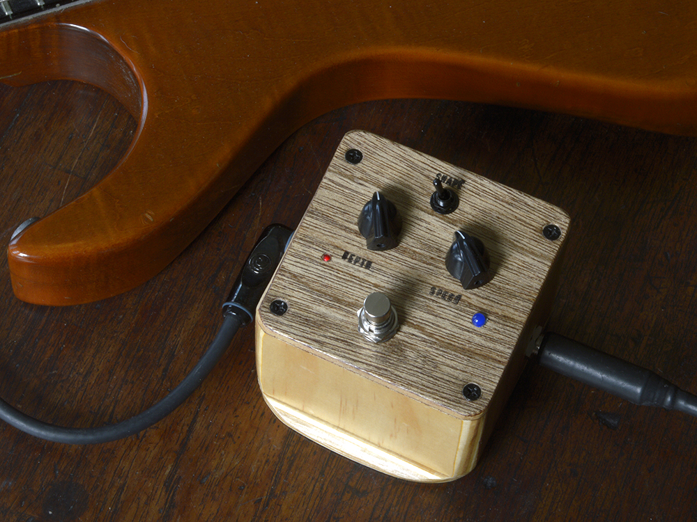 The MC Tremble Tremelo pedal with Black knobs and leads attached next to an electric guitar